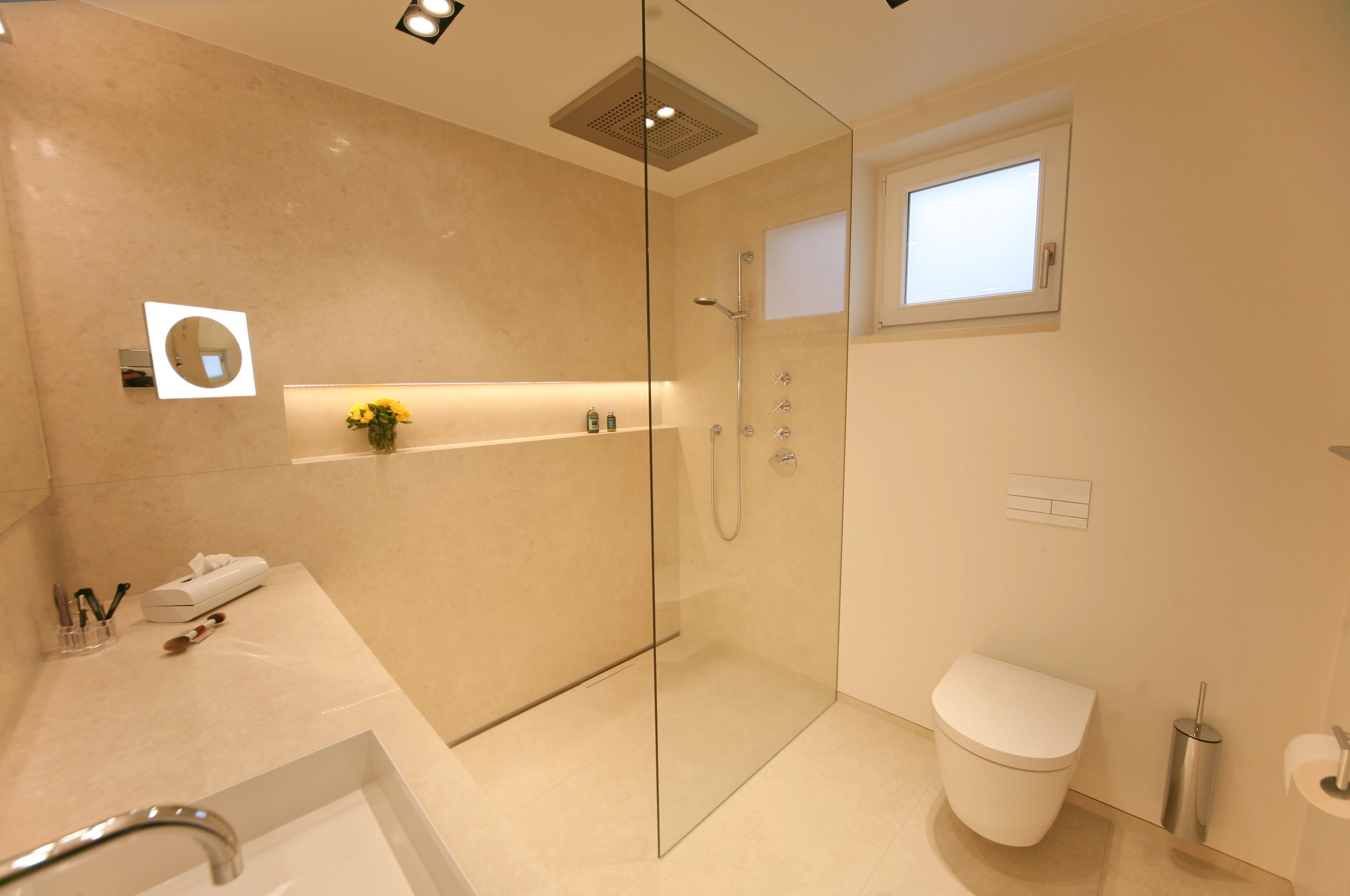 Luxuriöses Natursteinbad mit großzügiger Walk-in Dusche, moderner Regenbrause und stilvollem Waschtisch. Helles, minimalistisches Design mit eleganter Beleuchtung und klaren Linien.