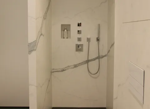 Begehbare Dusche mit Marmorverkleidung, integrierter Nische für Pflegeprodukte, moderner Handbrause und puristischer Armaturensteuerung in Chrom.