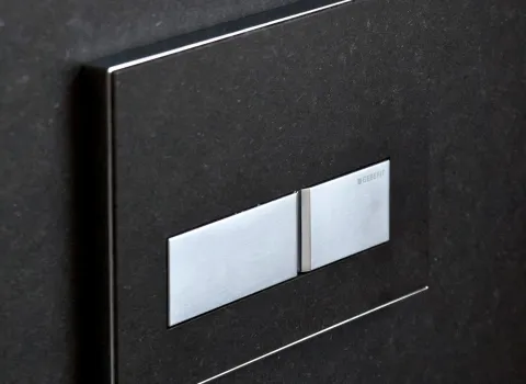 Edle Geberit Sigma50 Betätigungsplatte in Edelstahl auf dunklem Naturstein. Hochwertiges Detail für modernes Bad-Design mit klarer Eleganz.