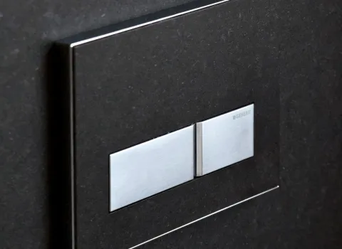 Edle Geberit Sigma50 Betätigungsplatte in Edelstahl auf dunklem Naturstein. Hochwertiges Detail für modernes Bad-Design mit klarer Eleganz.
