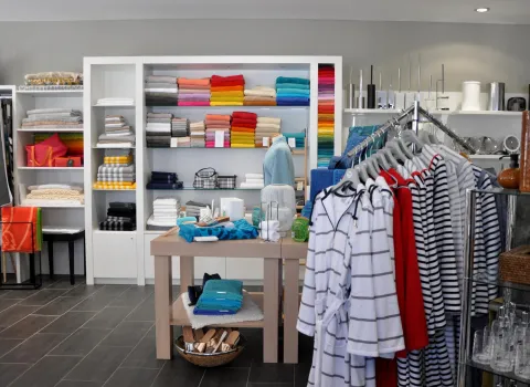 Innenansicht eines Geschäfts mit bunten Handtüchern, Bademänteln und Bad-Accessoires, ordentlich präsentiert in Regalen und auf Kleiderstangen.