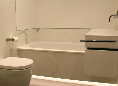 Modernes Badezimmer mit Marmoroptik, wandhängendem WC, Badewanne und elegantem Waschtisch mit Aufsatzwaschbecken.