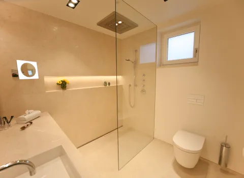 Luxuriöses Natursteinbad mit großzügiger Walk-in Dusche, moderner Regenbrause und stilvollem Waschtisch. Helles, minimalistisches Design mit eleganter Beleuchtung und klaren Linien.