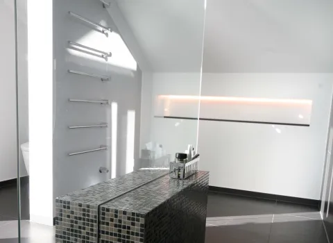 Stilvolles Dachbad mit moderner Walk-In-Dusche, edler Mosaik-Sitzbank und indirekter LED-Beleuchtung. Klare Linien und elegantes Design in dunklen Fliesen.