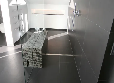 Modernes Dachbad mit großzügiger Walk-In-Dusche, eleganter Mosaik-Sitzbank und stilvollen dunklen Fliesen. Klare Linien für ein zeitloses Baddesign.
