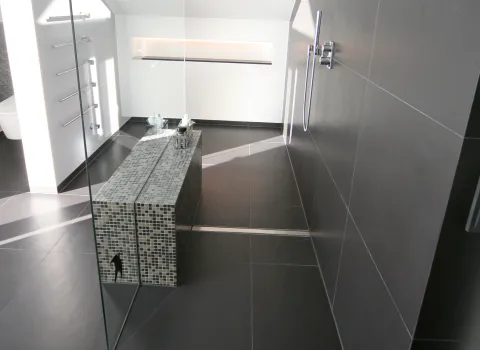 Modernes Dachbad mit großzügiger Walk-In-Dusche, eleganter Mosaik-Sitzbank und stilvollen dunklen Fliesen. Klare Linien für ein zeitloses Baddesign.