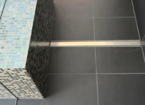 Detailaufnahme der bodengleichen Dusche im Dachbad mit edlem Mosaik-Design und moderner Ablaufrinne. Hochwertige Materialien für stilvolles Baddesign.