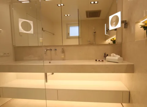 Zeitlos elegantes Natursteinbad mit großzügigem Waschtisch, beleuchtetem Spiegel und stilvoll integrierter LED-Ablage. Modernes Design für ein luxuriöses Badezimmerambiente.