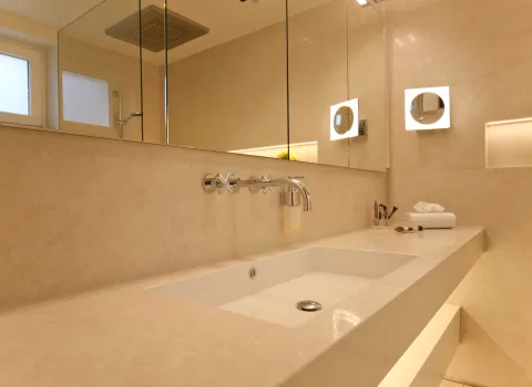 Moderner Naturstein-Waschtisch mit großem Spiegel, eleganter Beleuchtung und hochwertigen Armaturen. Zeitloses Badezimmerdesign mit klaren Linien und edler Oberfläche.