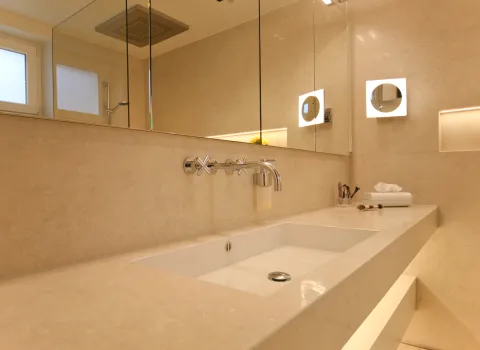 Moderner Naturstein-Waschtisch mit großem Spiegel, eleganter Beleuchtung und hochwertigen Armaturen. Zeitloses Badezimmerdesign mit klaren Linien und edler Oberfläche.