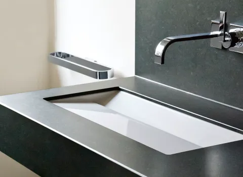 Moderner Waschtisch aus dunklem Naturstein mit eingelassenem Becken und eleganter Wandarmatur. Hochwertiges Design für exklusive Gäste-WCs.