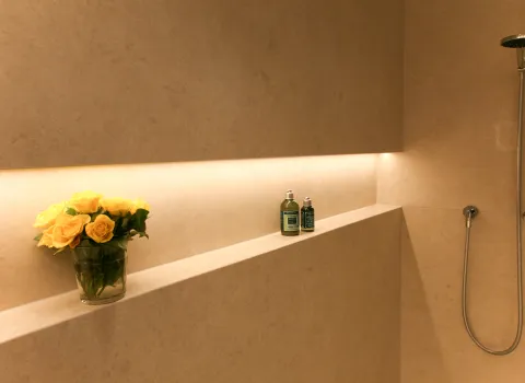 Detailaufnahme eines Natursteinbads mit integrierter Ablage, stilvoller LED-Beleuchtung und dekorativen Akzenten. Elegantes Zusammenspiel aus hochwertigem Naturstein, Accessoires und moderner Dusche