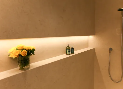 Detailaufnahme eines Natursteinbads mit integrierter Ablage, stilvoller LED-Beleuchtung und dekorativen Akzenten. Elegantes Zusammenspiel aus hochwertigem Naturstein, Accessoires und moderner Dusche