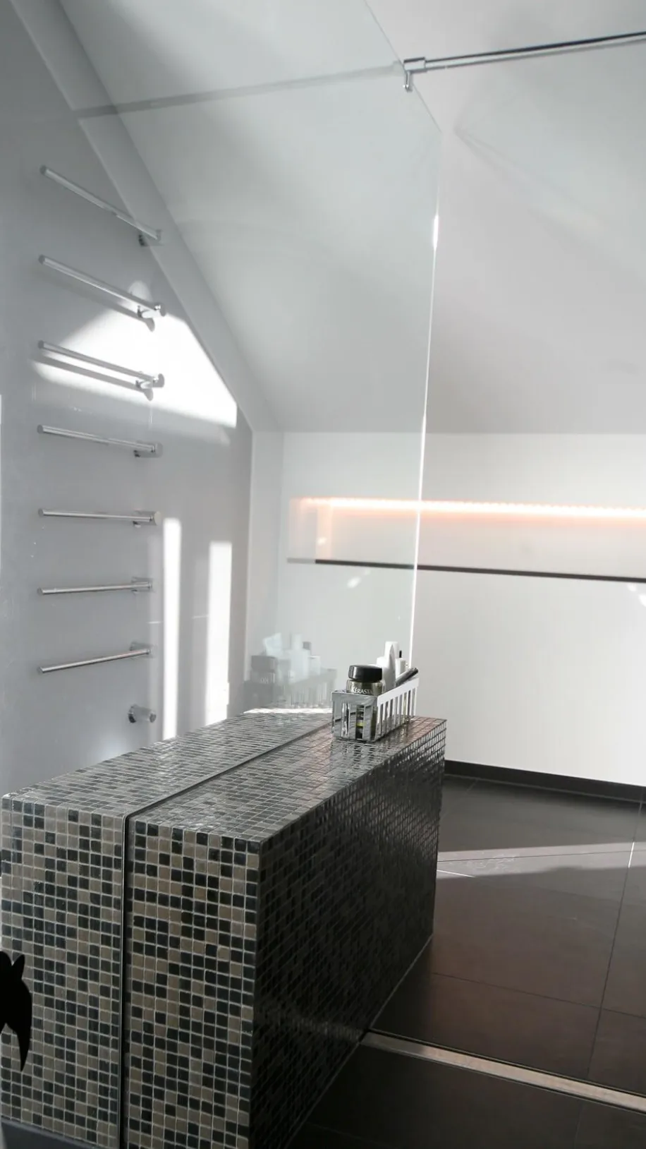 Stilvolles Dachbad mit moderner Walk-In-Dusche, edler Mosaik-Sitzbank und indirekter LED-Beleuchtung. Klare Linien und elegantes Design in dunklen Fliesen.