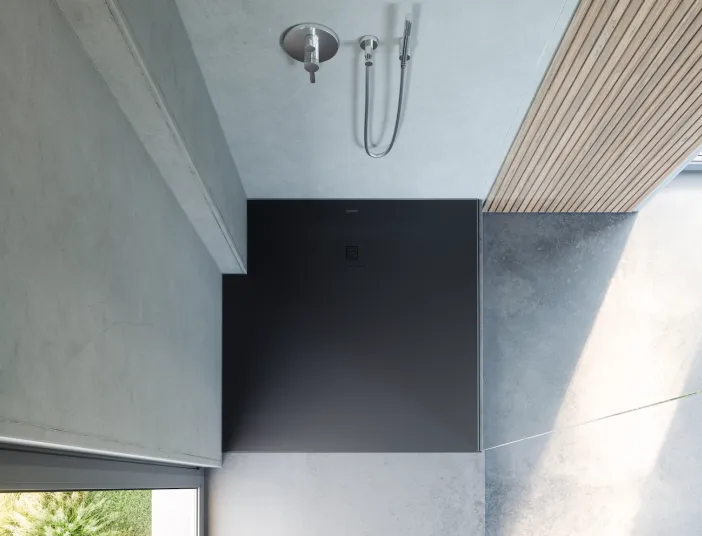 Moderne Dusche mit schwarzem Boden und minimalistischem Design in einem lichtdurchfluteten Badezimmer.